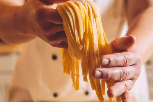 Mani che tengono tagliatelle fresche fatte a mano.