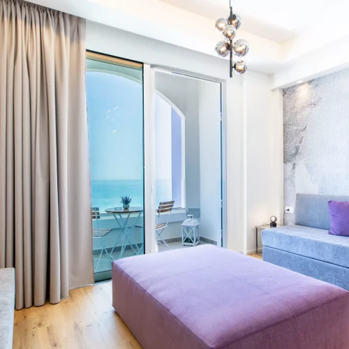 Soggiorno moderno con vista mare, arredato con divano grigio e pouf viola.