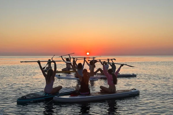 Persone su paddleboard al tramonto mentre alzano i remi.